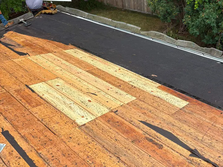 Lighter replacement boards visible among exposed roof decking