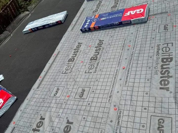 Synthetic roof underlayment beside a dark eave layer and shingle bundles
