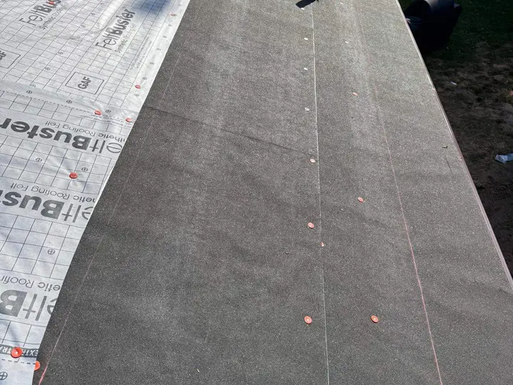 Rows of capped fasteners on dark roof underlayment beside a synthetic layer